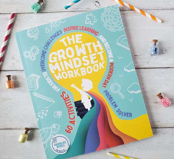 The Growth Mindset Workbook on white wood with straws and bottles of colored salts
