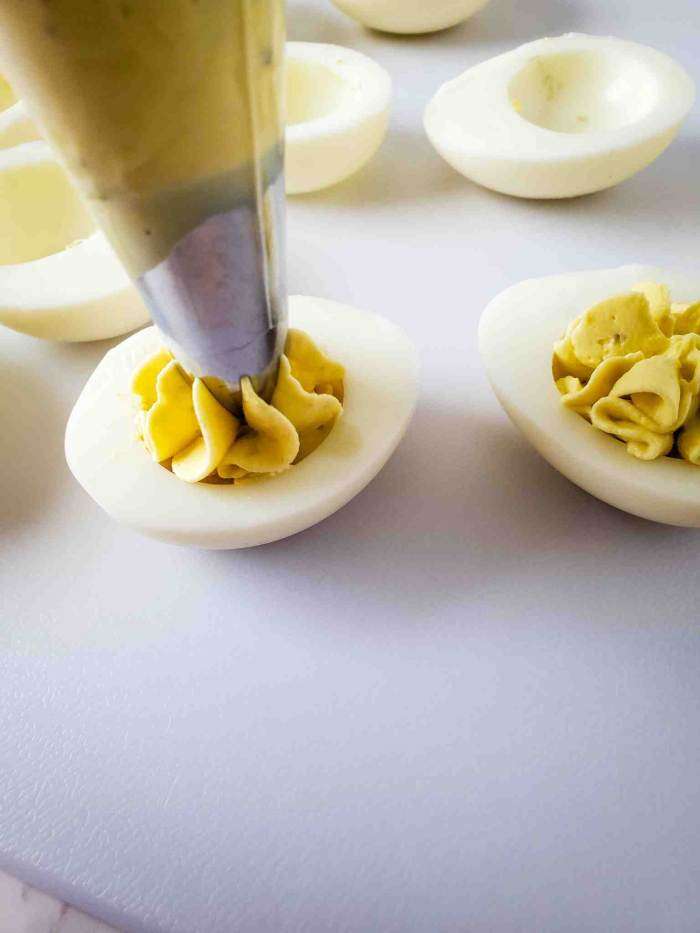 a piping bag adding the deviled egg mixture to the egg