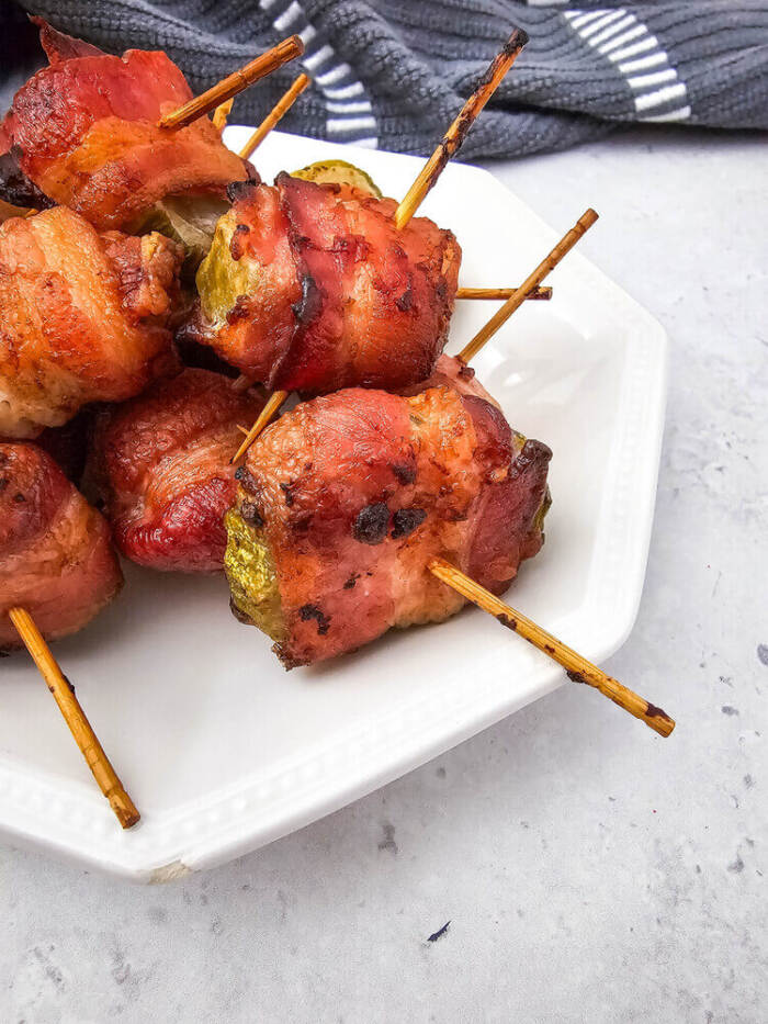 Air Fryer Bacon Wrapped Pickles on a white plate with a gray towel in the background