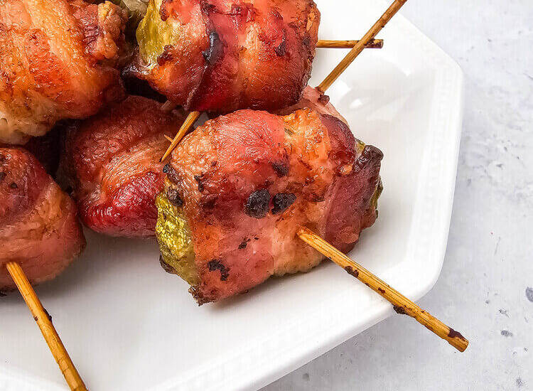 Air Fryer Bacon Wrapped Pickles on a white plate with a gray towel in the background