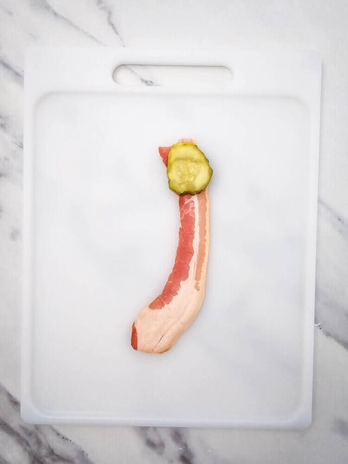 a piece of pickle being wrapped in bacon