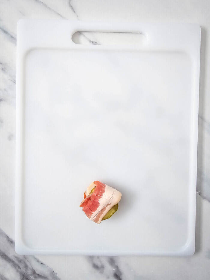 pickle wrapped in bacon on a cutting board