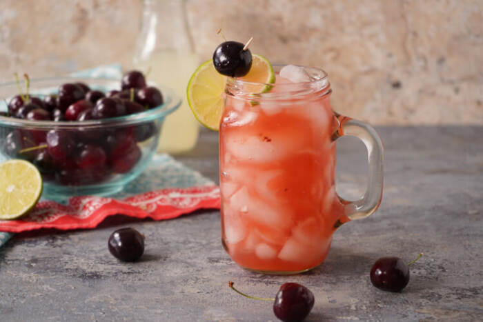 Cherry Lemonade Cocktail in a glass with cherries in a bowl