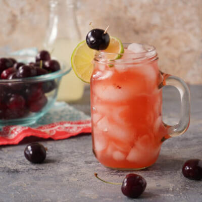 Cherry Lemonade Cocktail in a glass with cherries in a bowl
