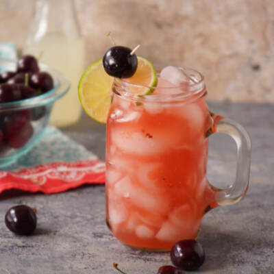 Cherry Lemonade Cocktail in a glass with cherries in a bowl