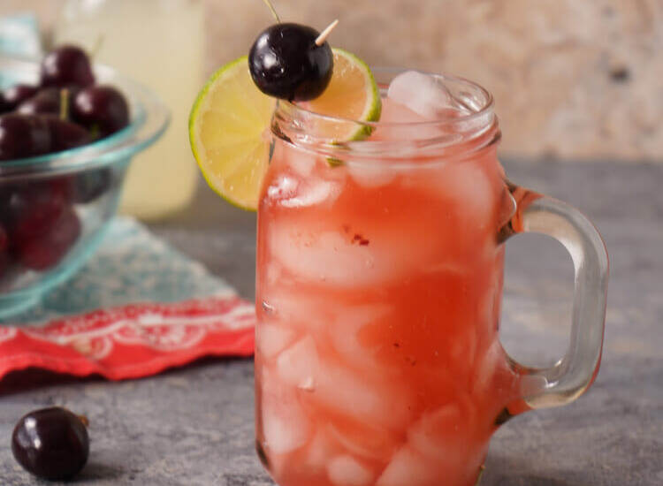 Cherry Lemonade Cocktail in a glass with cherries in a bowl