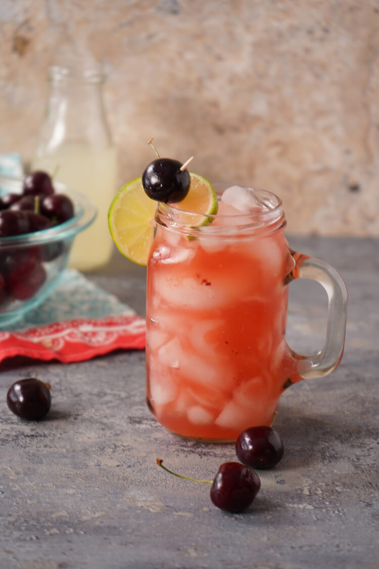 Cherry Lemonade Cocktail in a glass with cherries in a bowl