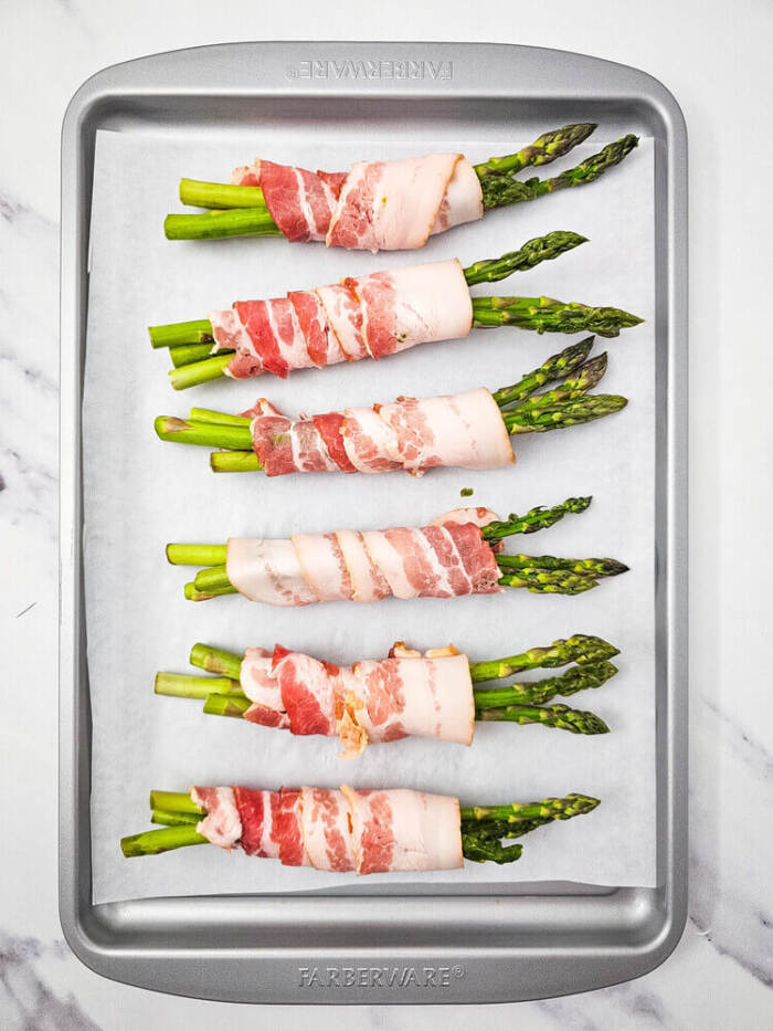 asparagus wrapped in bacon on a baking sheet
