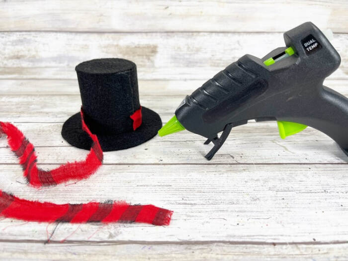 Black felt snowman hat with a red plaid band being glued together using a hot glue gun.