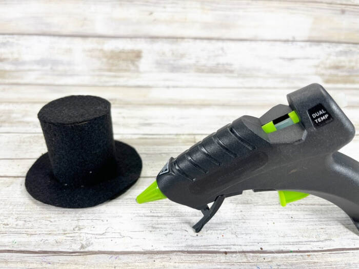 Black craft felt pieces and a cardboard toilet paper tube arranged with a hot glue gun, ready to assemble a snowman hat.