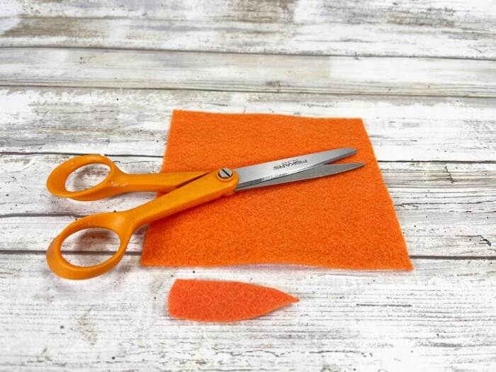 Orange craft felt square with scissors and a small carrot shape cut out on a wooden surface.