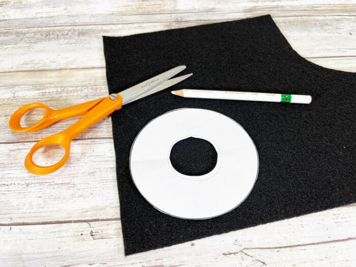 Snowman hat brim pattern traced onto black craft felt with scissors and pencil nearby.