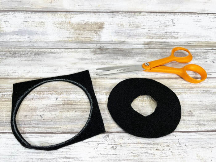 Black felt hat brim pieces cut out and placed on a wooden work surface with scissors.