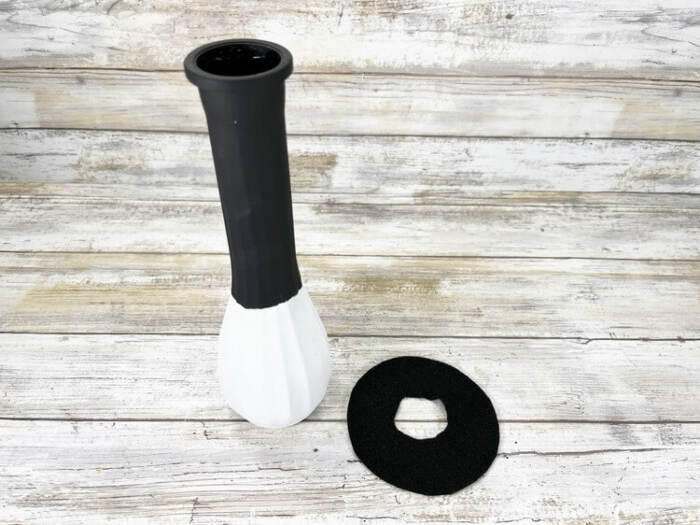 Fully painted vase with black top section drying next to black acrylic paint and a brush.