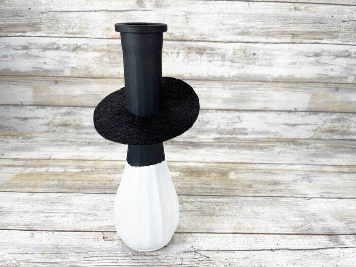 Black felt hat brim placed beside the painted vase, ready to be attached.
