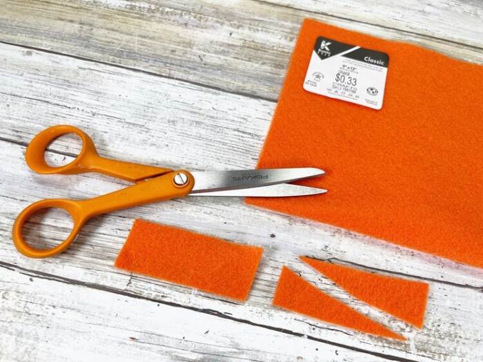 Orange craft felt being cut into carrot nose shapes with scissors.
