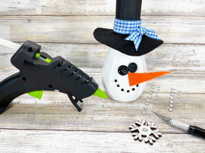 Finished Snowman Vase Craft with painted snowflake accents and craft supplies nearby.