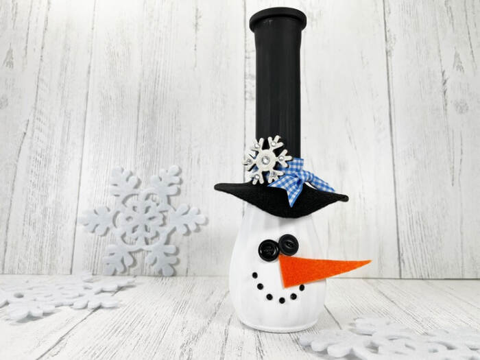 Snowman Vase Craft made from a painted glass vase with a black top hat, orange felt carrot nose, button face, and winter decor background.