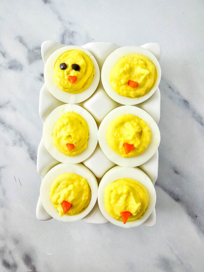 Decorating Easter Chick Deviled Eggs with olive eyes and carrot beaks.