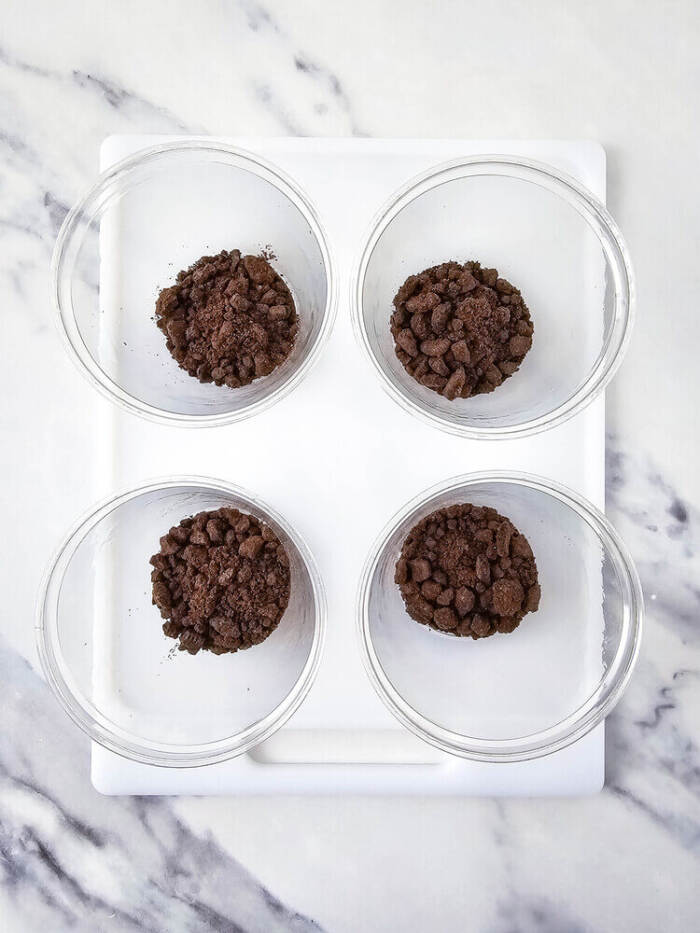 Crushed chocolate cookies added to clear cups for Easter Peeps Dirt Cups.