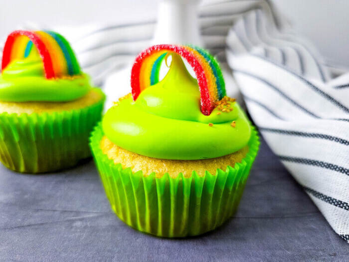 St. Patrick’s Day cupcakes with rainbow candy arches and sprinkles on a white plate.