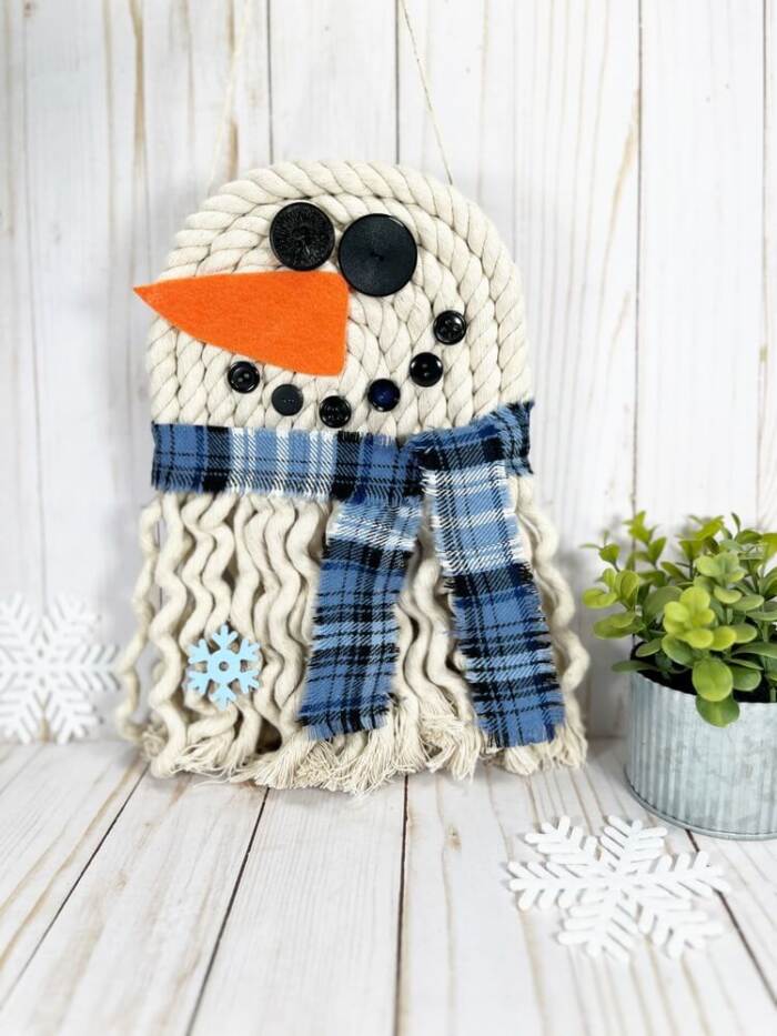 DIY rope snowman decoration hanging on white wood background.