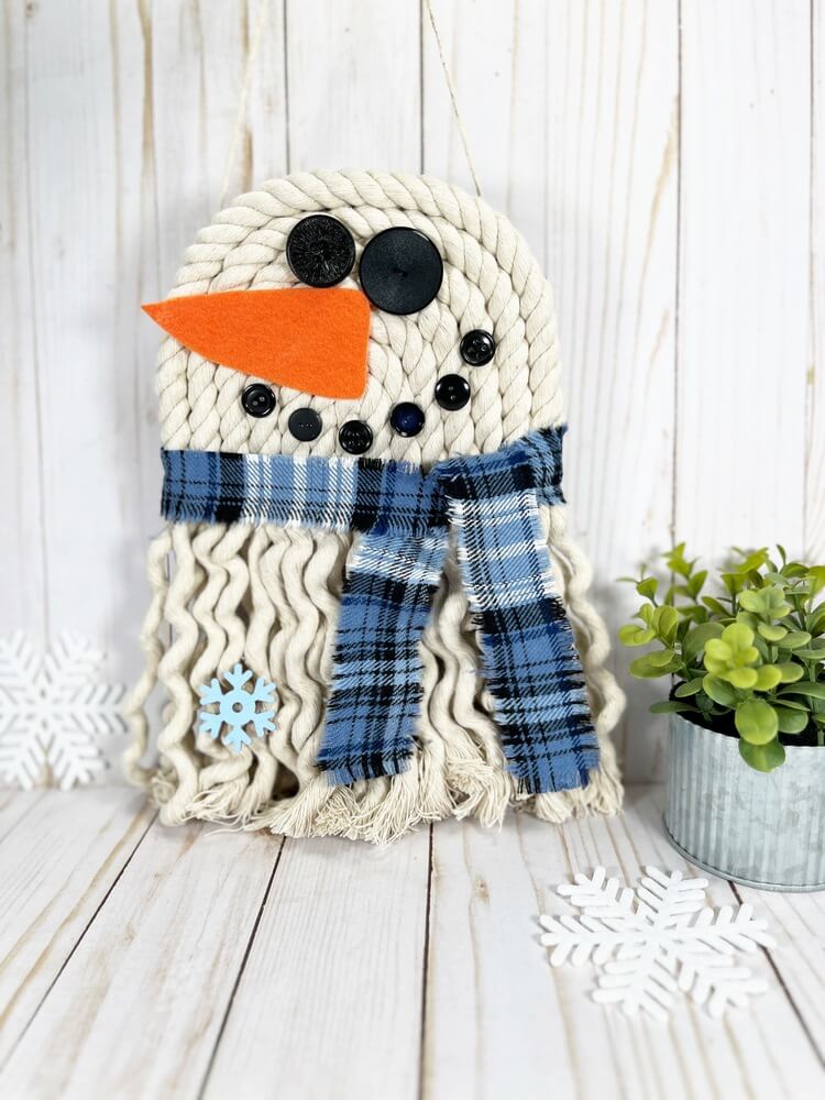 DIY rope snowman decoration hanging on white wood background.