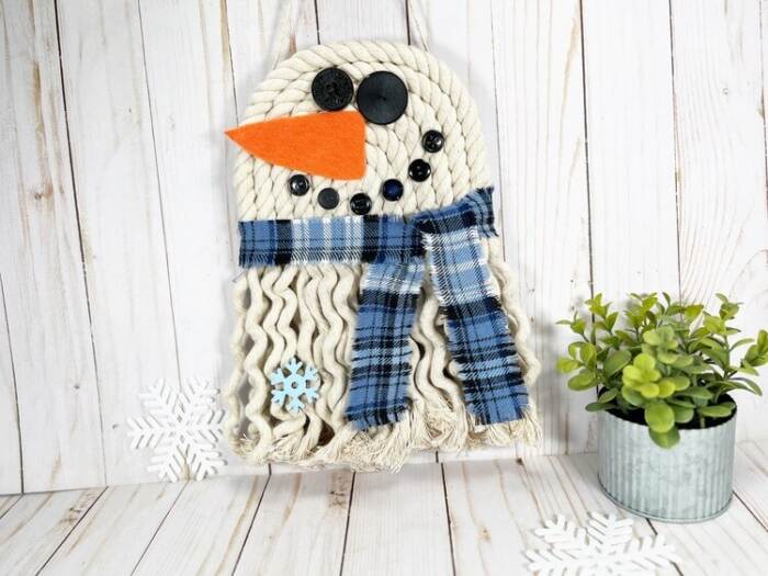 Rope snowman with scarf and carrot nose on rustic background.