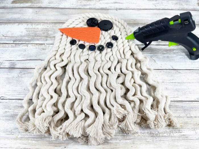 gluing felt carrot nose and button eyes onto rope snowman