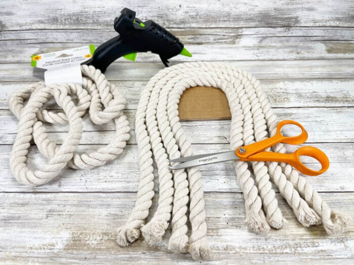 Snowman rope craft with scissors and glue gun on work surface.