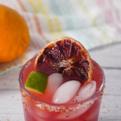 Close up of blood orange margarita showing ice, lime wedge, and dried blood orange slice garnish.