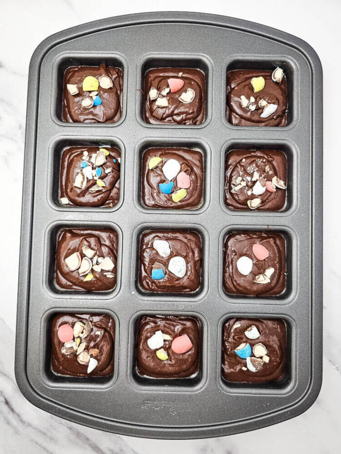 Brownie batter divided into brownie pan cavities with candies