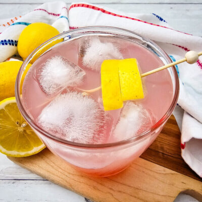 A glass of watermelon Jolly rancher drink garnished with lemon slices.