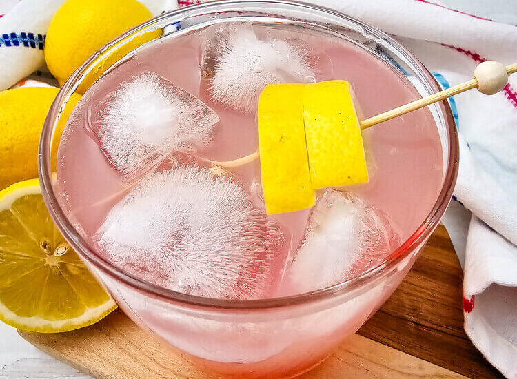 A glass of watermelon Jolly rancher drink garnished with lemon slices.