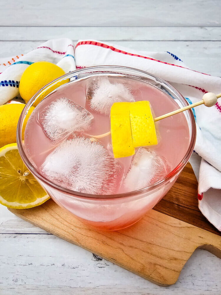 A glass of watermelon Jolly rancher drink garnished with lemon slices.