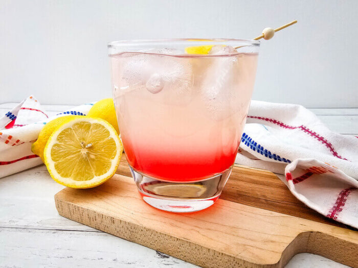 A glass of watermelon Jolly rancher drink beside a sliced lemon.