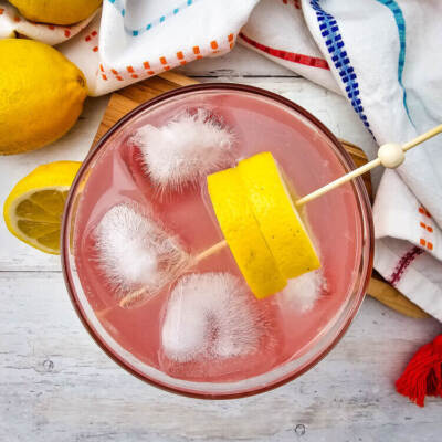 A glass of watermelon Jolly rancher drink with slices of lemon on top.