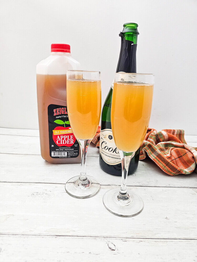 Two champagne flutes filled with champagne and apple cider for apple cider mimosas recipe.