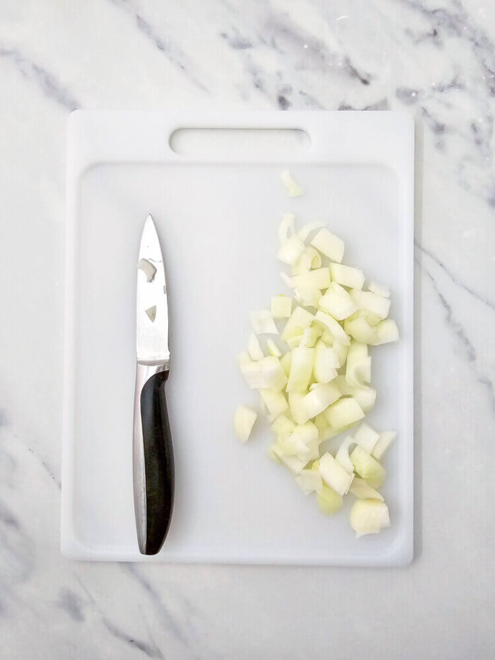 Diced onion on a chopping board for biscuit pizza casserole.