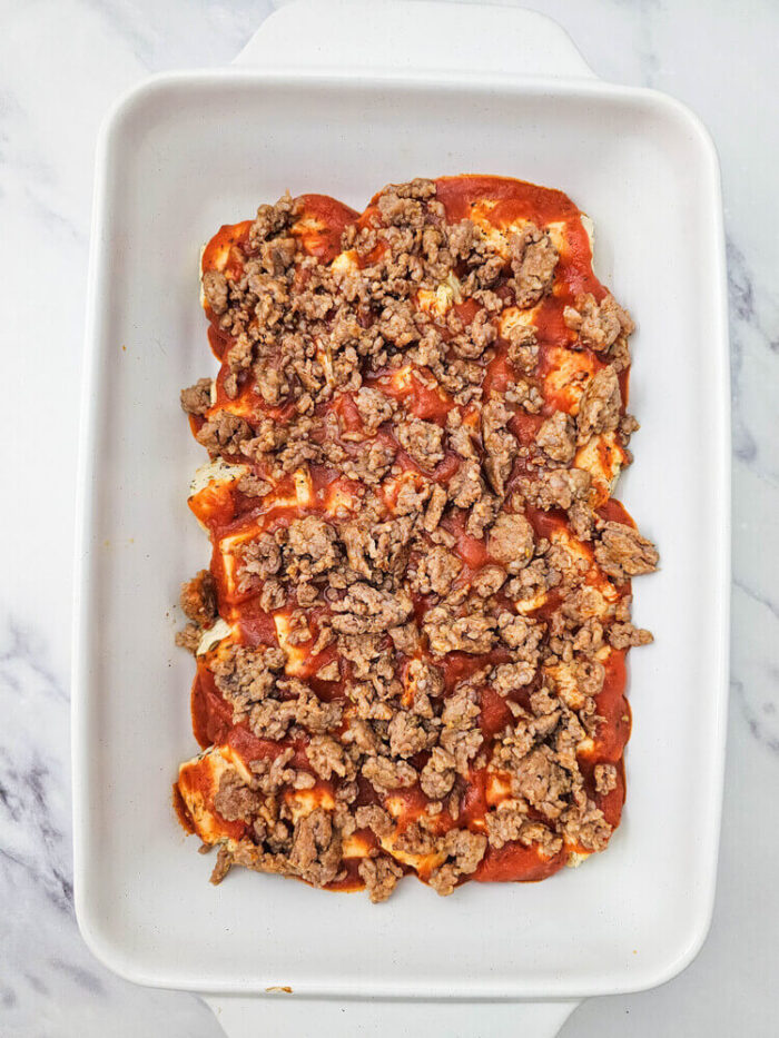 Baked biscuits topped with sauce and sausage for biscuit pizza casserole.
