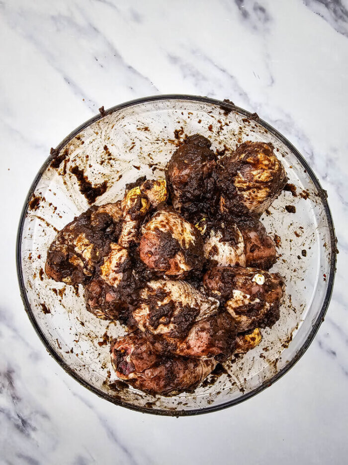 A bowl with chicken coated with seasoning for jerk chicken drumsticks recipe.